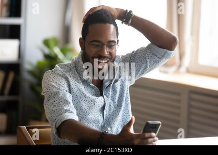 Uomo africano che tiene smartphone leggere notizie incredibili si sente eccitato Foto Stock