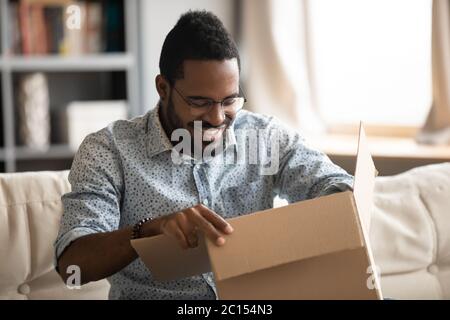 Uomo africano apertura pacco seduto sul divano a casa Foto Stock