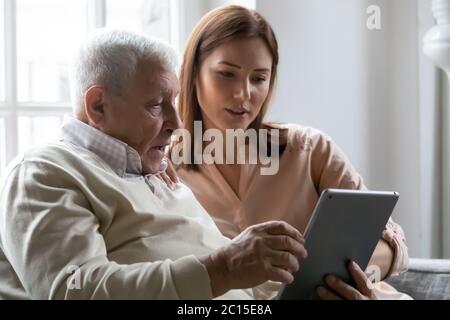 Figlia di ringhiup che si prende cura insegnando il padre anziano ad usare la tavoletta Foto Stock