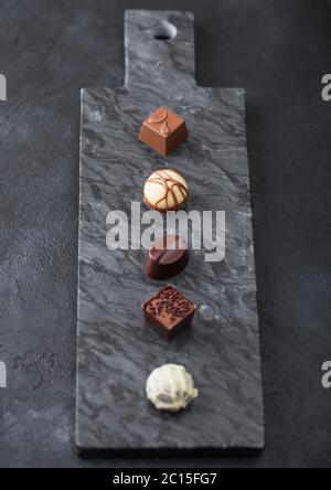 Il lusso di cioccolatini selezione sul pavimento di marmo nero a bordo. Bianco, cioccolato fondente e al latte assortimento. Vista superiore Foto Stock