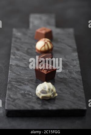 Il lusso di cioccolatini selezione sul pavimento di marmo nero a bordo. Bianco, cioccolato fondente e al latte assortimento. Vista superiore Foto Stock