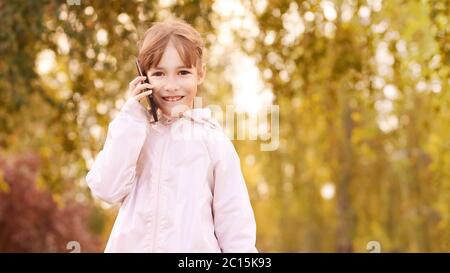 La bambina parla telefono. Sfondo autunno Foto Stock