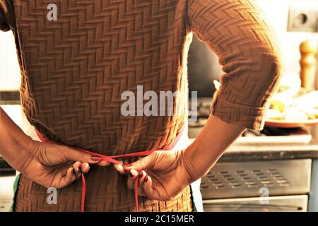 Retro lato di donna che indossa grembiule preparare per cucinare in cucina Foto Stock