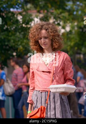 Giovane bella donna cammina in un parco che tiene in mano un contenitore di plastica con cibo di strada in una mano Foto Stock