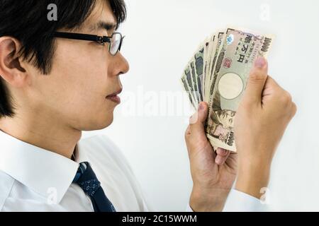 Giovane uomo d'affari giapponese che conta soldi. Tenere una pila di banconote giapponesi Yen. Isolato su bianco. Foto Stock