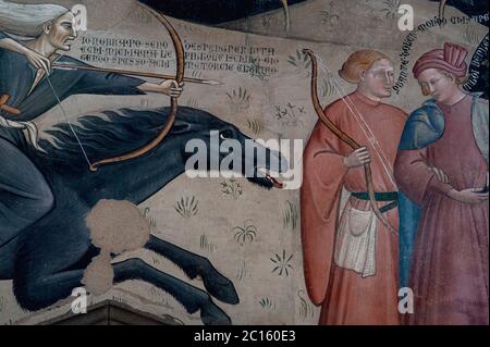 Il cacciatore di mirini, cavalcando a cavallo nero, rappresenta la pandemia della peste della morte Nera che si estenuava in 1300s Europa mentre punta a una freccia contro due ignari cacciatori di nobile nascita. Trionfo dell'affresco della morte, dipinto intorno al 1380, dal pittore senese Bartolo di Fredi (c. 1330-1410). Nella Chiesa di San Francesco a Lucignano, Toscana, Italia. Foto Stock
