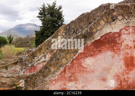 Una vista attraverso le mura rovinate, alcune ancora ricoperte di intonaco colorato, attraverso il Vesuvio, nell'antica città di Pompei, Campania, Italia Foto Stock