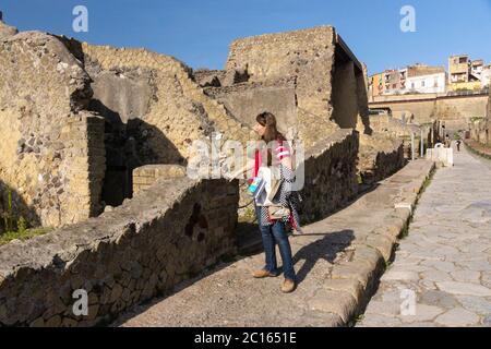 Una donna turistica su un sentiero che esplora la via Cardo V inferiore (inferiore) nell'antica città romana di Ercolano, patrimonio dell'umanità dell'UNESCO Foto Stock