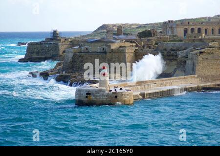 VALLETTA, MALTA - DEC 31, 2019: Vista da Fort St Elmo sul Grand Harbour Ricasoli East Breakwater e faro rosso durante le onde forti Foto Stock