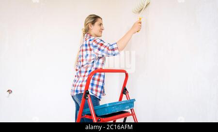 Bella giovane donna che fa il rinnovamento a casa e dipinge le pareti con rullo Foto Stock