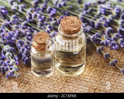 Due bottiglie di vetro di olio essenziale di lavanda e lavanda fresca profumata su uno sfondo di juta sackcloth. Concetto di spa, bellezza, cura della pelle e cosmetologia Foto Stock