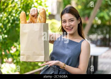 Ritratto di attraente e sorriso asiatico donna che tiene borsa della spesa acquistare dal supermercato. Concetto di acquisto di cibo e bevande e consumismo. Foto Stock