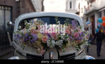 Quito, Pichincha / Ecuador - Giugno 22 2019: Sistemazione di rose rosse e gialle sul cofano di una vecchia auto bianca parcheggiata su una strada piena di persone walki Foto Stock