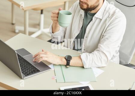 Vista ad angolo alto sull'uomo adulto che beve caffè mentre usa il laptop in un ambiente interno minimo, spazio per la copia Foto Stock