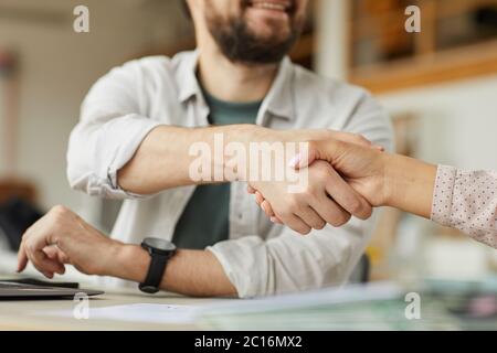 Primo piano di un uomo sorridente che scuote le mani con un collega in un ambiente di ufficio minimo, spazio per la copia Foto Stock