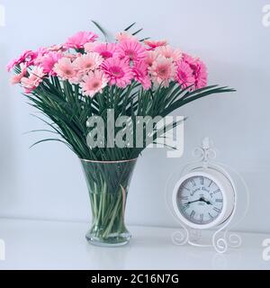 Primo piano sveglia bianca retrò e bouquet di fiori in vaso di vetro sul tavolo. Sfondo bianco. Vita morta. Foto Stock