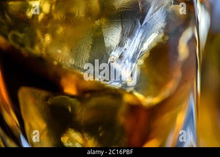 Pezzi di cubetto di ghiaccio in whiskey. Primo piano macro di cubetti di ghiaccio in una bevanda di vetro o un altro alcool. Sfondo texture astratto Foto Stock