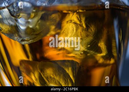 Pezzi di cubetto di ghiaccio in whiskey. Primo piano macro di cubetti di ghiaccio in una bevanda di vetro o un altro alcool. Sfondo texture astratto Foto Stock