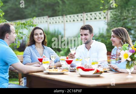 Felici amici che tostano bicchieri di vino in giardino mentre si pranzano Foto Stock