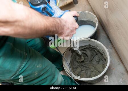 Un addetto alla costruzione mescola un adesivo speciale per piastrelle. Miscelatore adesivo a base di cemento denso. Foto Stock