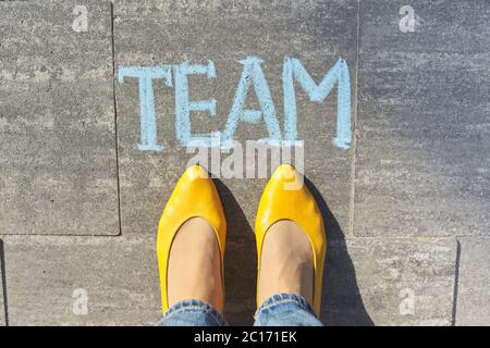 Concetto di squadra, vista dall'alto sulle gambe della donna e testo scritto in gesso sul marciapiede grigio Foto Stock