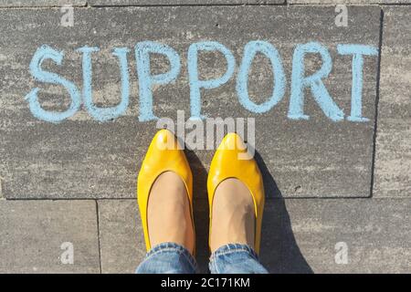 Concetto di supporto, vista dall'alto sulle gambe della donna e testo scritto in gesso sul marciapiede grigio Foto Stock