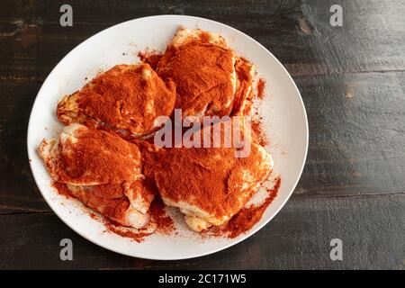 Cosce di pollo condite con Paprika per il pollo Paprikash: Cosce di pollo crude cosparse di paprika dolce ungherese e pimenton (paprika affumicata) Foto Stock