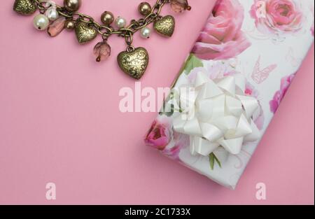 Sfondo con cuore d'oro e collana di perle, regalo di rosa avvolto presente isolato su rosa Foto Stock