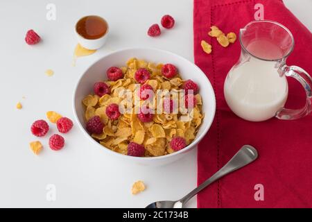 Cereali per la prima colazione di cornflakes, lamponi e miele e latte su sfondo bianco Foto Stock