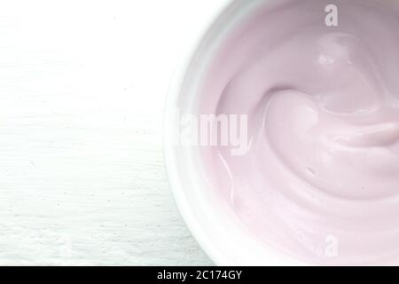 Yogurt cremoso di frutta al raspberry di colore naturale in recipiente di vetro bianco su tavola di legno bianco in primo piano Foto Stock