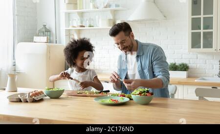 Il padrino insegna la figlia africana tagliare diverse verdure per insalata vegetariana Foto Stock