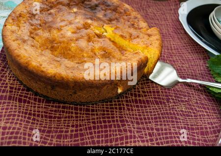 Torta su una tovaglia di colore borgogna. Un pezzo di torta viene preso con una spatola Foto Stock