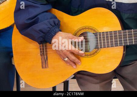 Avvicinati alla mano di un anziano seduto con una chitarra vestita con una camicia blu con un anello sul dito Foto Stock