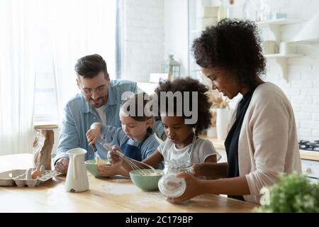 I piccoli aiutanti e i genitori cucinano insieme la torta in cucina Foto Stock