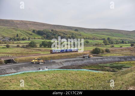 Northern Rail classe 158 Sprinter treno che passa la costruzione del trasporto di merci vagliando per Arcow Quarry a Helwith Bridge, Yorkshire, Regno Unito Foto Stock