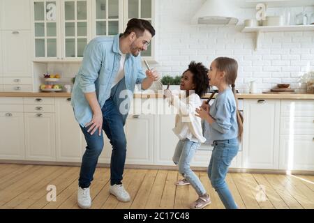 Papà con figlie che si divertono a ballare e a cantare in cucina Foto Stock