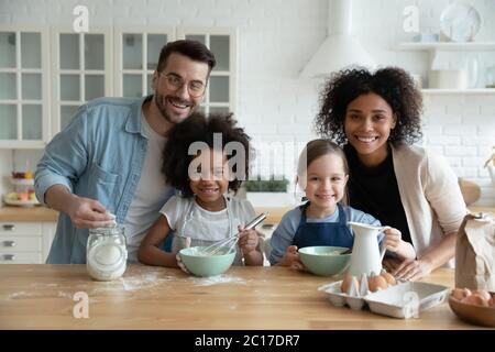 Famiglia multietnica con figlie impegnate nella preparazione di torte in cucina Foto Stock