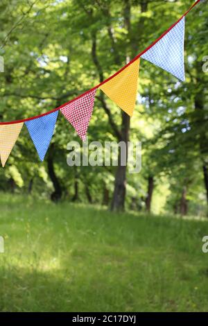 Bandiere colorate e triangolari appese tra gli alberi. Festa estiva in giardino. Decorazioni per matrimoni o compleanni all'aperto. Metà estate, festa junina Concept Foto Stock