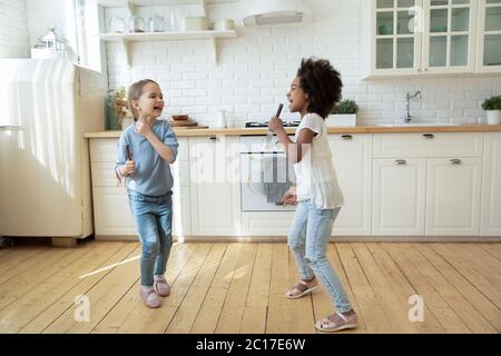 Le ragazze multietniche giocano in cucina cantando canzoni e ballando Foto Stock