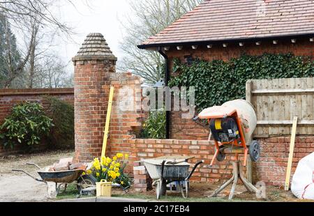 Lavori di costruzione con attrezzi e betoniera, costruendo un muro di giardino di mattoni fuori di una casa britannica Foto Stock