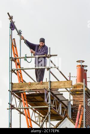 Operaio di costruzione su una torre di impalcatura sopra un tetto durante la riparazione della casa nel Regno Unito Foto Stock