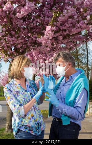 Coppia senior che indossa maschere chirurgiche e guanti all'aperto in primavera durante la pandemia del coronavirus in piedi guardando gli occhi l'uno verso l'altro con lo Foto Stock