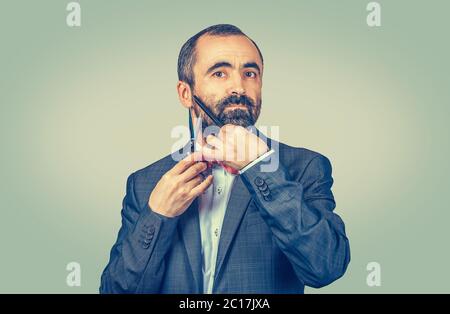 Parrucchiere con bearato, stilista barbiere che taglia la sua barba con forbici e pettine, indossando un'elegante giacca con cravatta rossa. Uomo adulto di stile Foto Stock