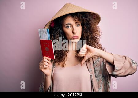 Bella donna turistica con capelli ricci e piercing che indossa cappello asiatico tenendo passaporto giapponese con faccia arrabbiata, segno negativo che mostra dispiacere con il thum Foto Stock