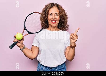 Giovane età bella sportivo che gioca a tennis tenendo racchetta e palla su sfondo bianco sorridente felice puntando con mano e dito a lato Foto Stock