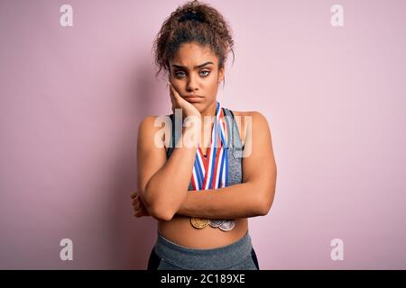 Giovane afroamericano sportivo ragazza facendo sport vincere medaglie su isolato sfondo rosa pensando stanco e annoiato con problemi di depressione Foto Stock