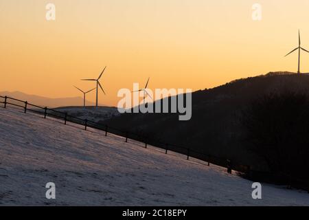 La silhouette dei mulini a vento sulla cima di una montagna da lontano con il cielo arancione del tramonto. Foto Stock