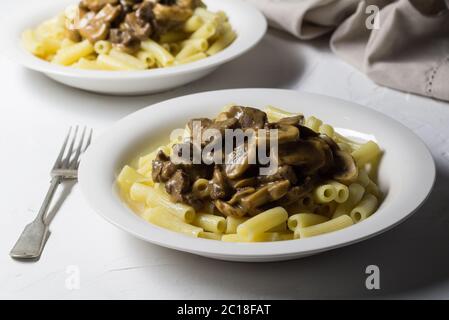 Supper plates with thick creamy mushroom and beef stroganoff on pasta and rustic white background Stock Photo
