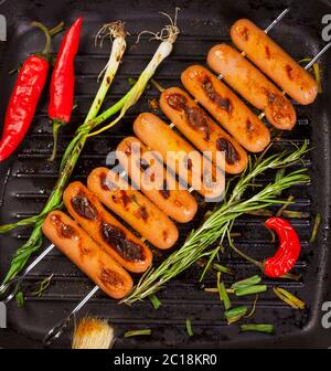 Salsicce fritte con erbe, spezie e verdure in una padella da vicino. Foto Stock