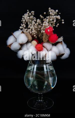 bicchiere d'acqua e bouquet di cotone e fiori bianchi su fondo nero Foto Stock